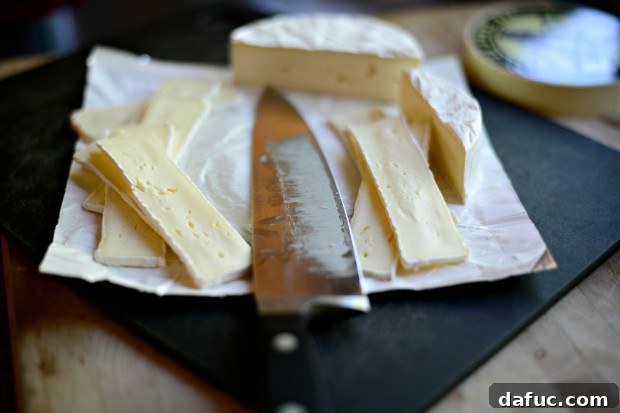 Thin slices of brie cheese, arranged in an appealing pattern on a cutting board, prepared for the flatbread.