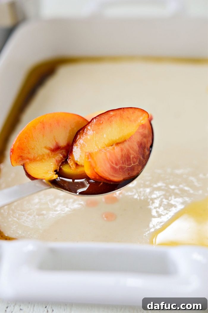 Spoonfuls of cooked peaches and their juices being scattered over the batter and brown butter in the baking dish