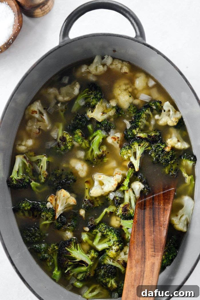 Chicken broth being poured into a pot with roasted vegetables