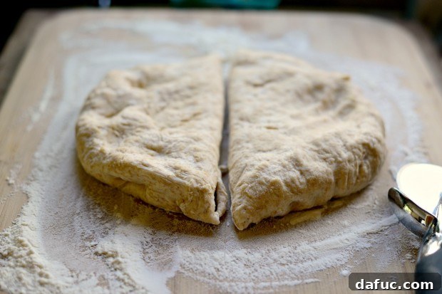Pillowy Naan Perfection at Home 24 Naan dough on a floured surface, cut in half with a pizza cutter.