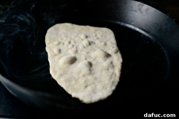 Pillowy Naan Perfection at Home 30 Rolled naan dough laid into a hot, buttered cast iron skillet to begin cooking.