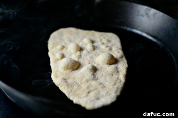 Pillowy Naan Perfection at Home 31 Naan bread cooking in a skillet, showing visible bubbles forming on the surface.