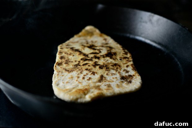 Pillowy Naan Perfection at Home 32 Naan bread flipped in the skillet, revealing a golden brown and bubbly bottom.