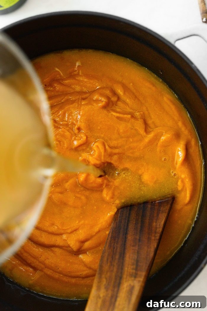 Vibrant Sweet Potato Tomatillo Bisque 15 Pureed soup being transferred to a Dutch oven with additional broth