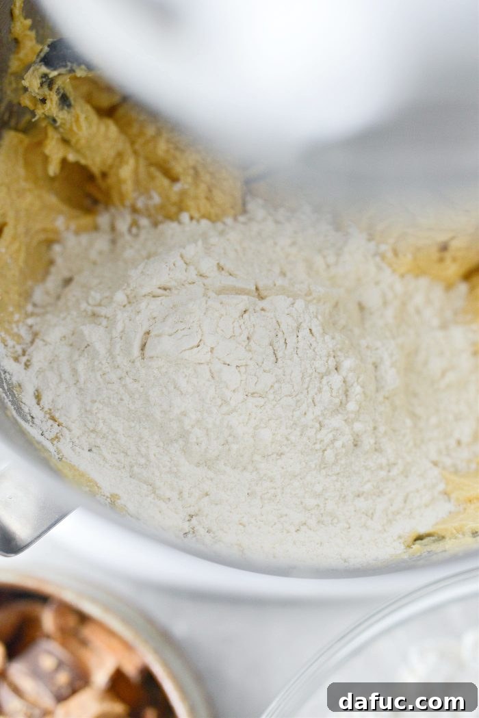 Dry ingredients being gradually added to the wet cookie dough mixture in the stand mixer.