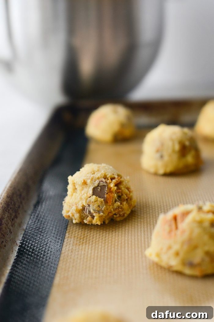 Cookie dough being scooped onto a prepared baking sheet using a 2-tablespoon scoop.