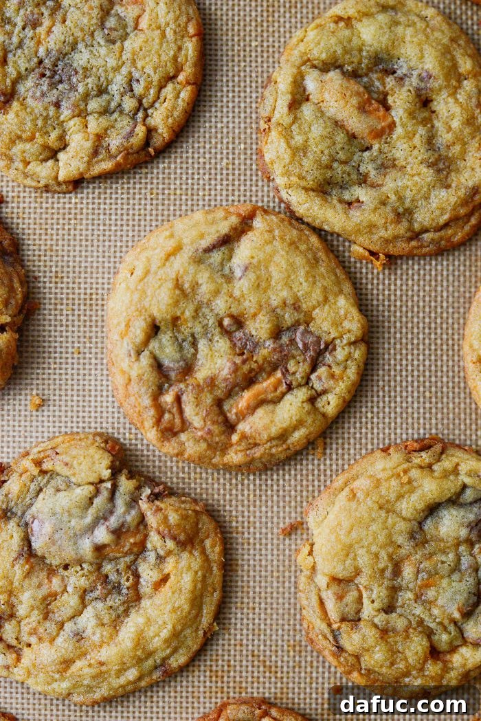 Freshly baked Butterfinger Cookies cooling on a baking sheet, with golden edges.