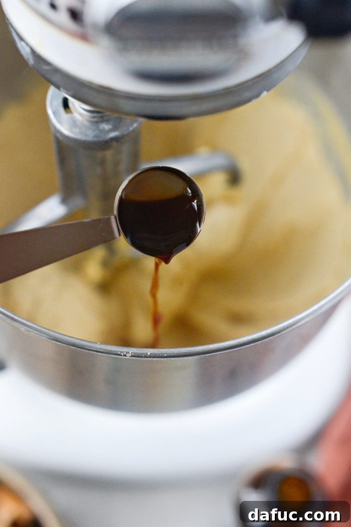 Pure vanilla extract being poured into the stand mixer bowl.