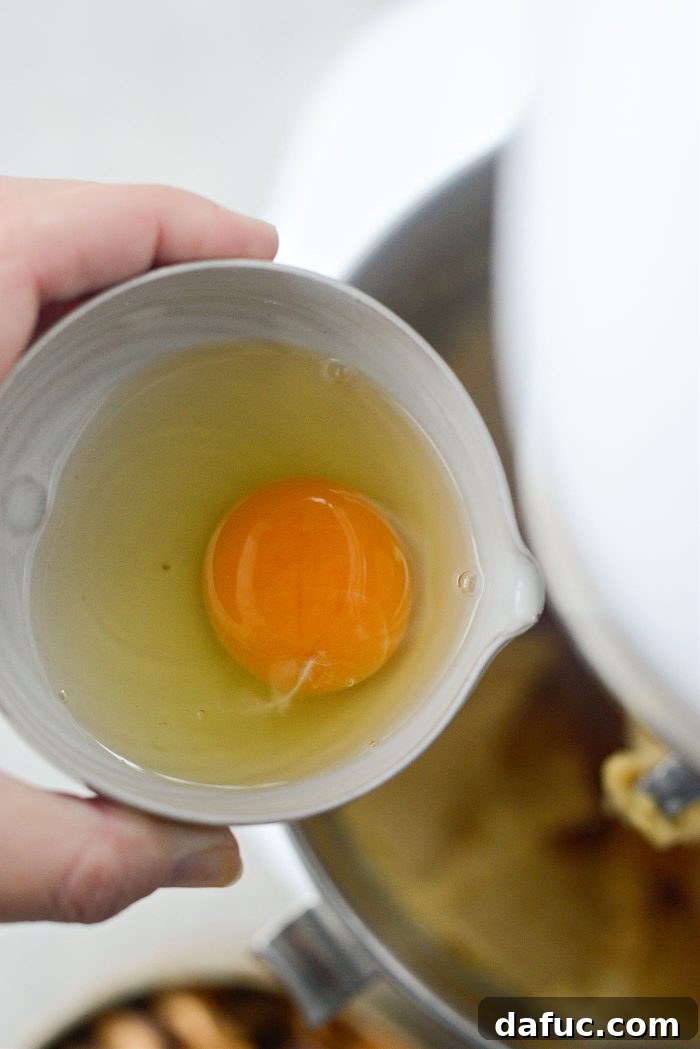 An egg being added to the mixture in the stand mixer bowl, one at a time.