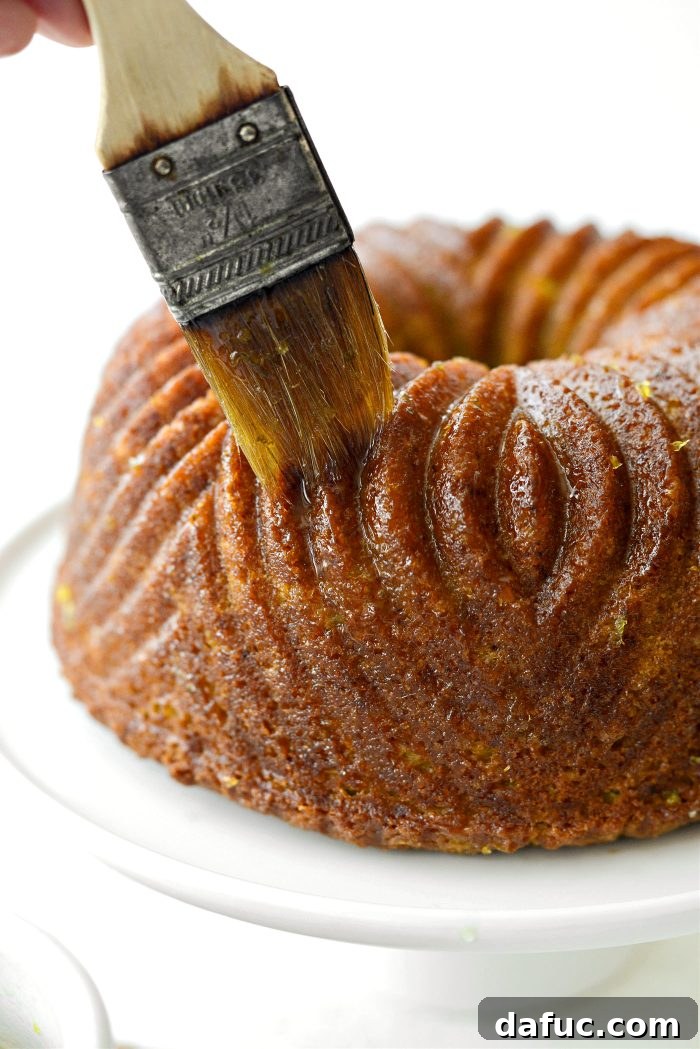 Brushing the remaining lemon-lime glaze over the entire surface of the bundt cake, ensuring full coverage and shine.