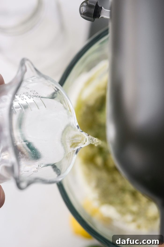 Pouring water into the cake batter mixture in the stand mixer.