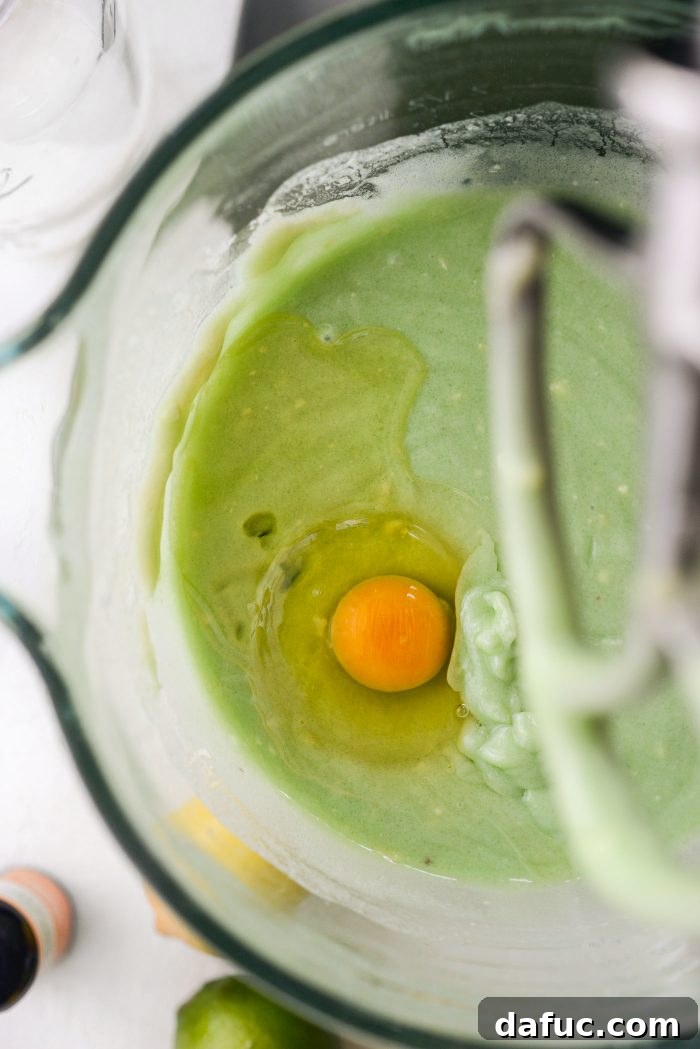 Adding one large egg at a time to the cake batter for optimal incorporation.