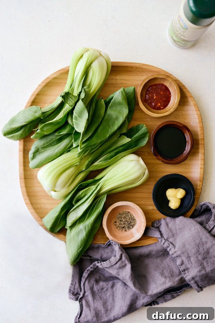 Fresh ingredients for grilled baby bok choy and ginger chili sauce laid out on a bamboo tray, including whole bok choy, ginger, and chili paste