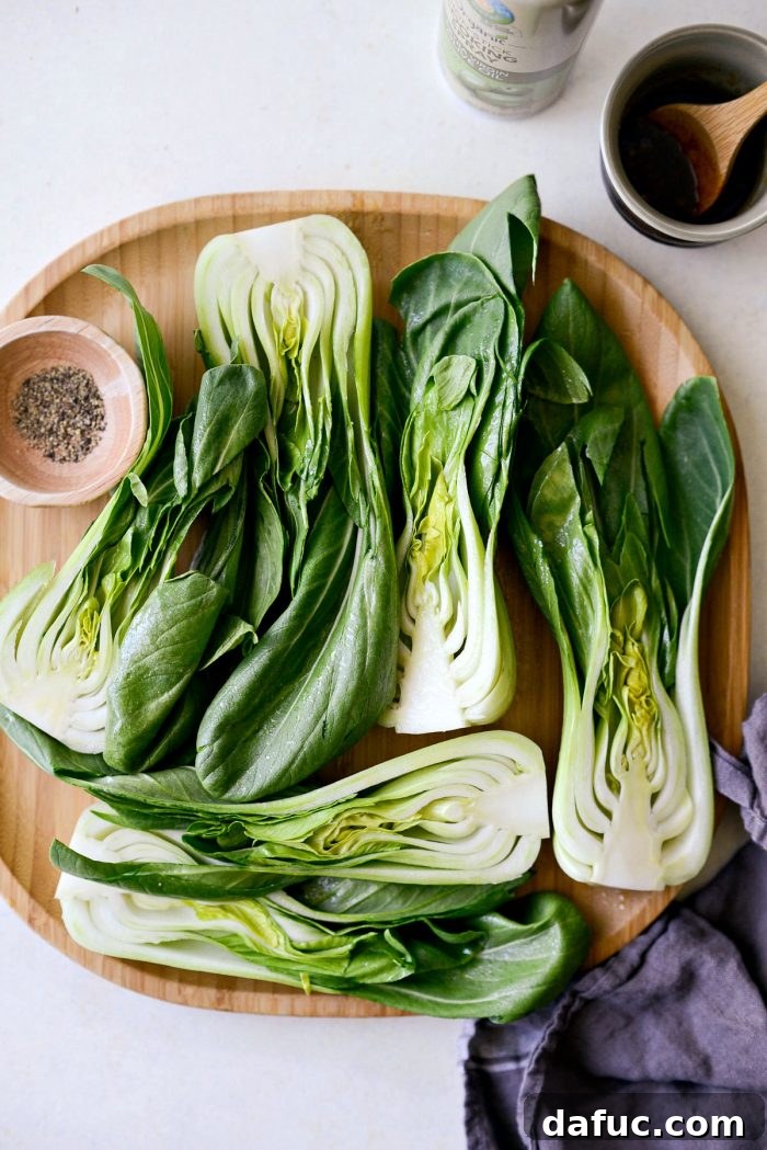 A bamboo tray displaying several halves of fresh baby bok choy, meticulously cleaned and ready for grilling