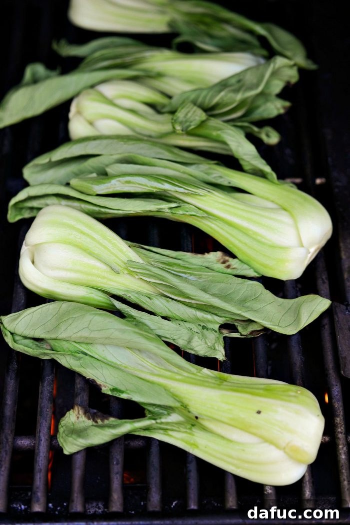 Baby bok choy placed cut-side down on a hot grill grate, showing early grill marks