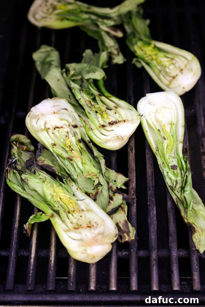 Grilled baby bok choy showing beautiful char marks after being flipped, continuing to cook
