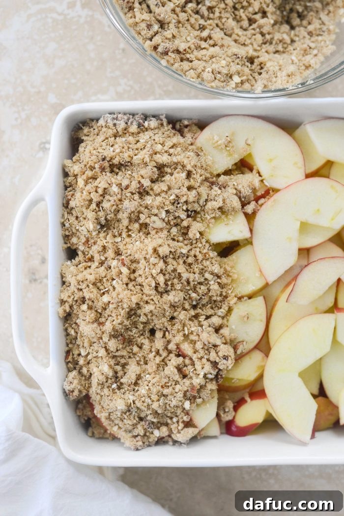 Effortless Apple Crumble 11 Oat topping sprinkled generously over the sliced apples in the baking dish, before baking.