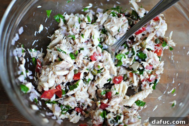 mix A spoon stirring the colorful tuna mixture in a bowl.
