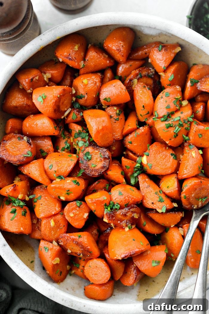 Two serving dishes filled with Maple Glazed Carrots, garnished with fresh herbs, on a wooden table