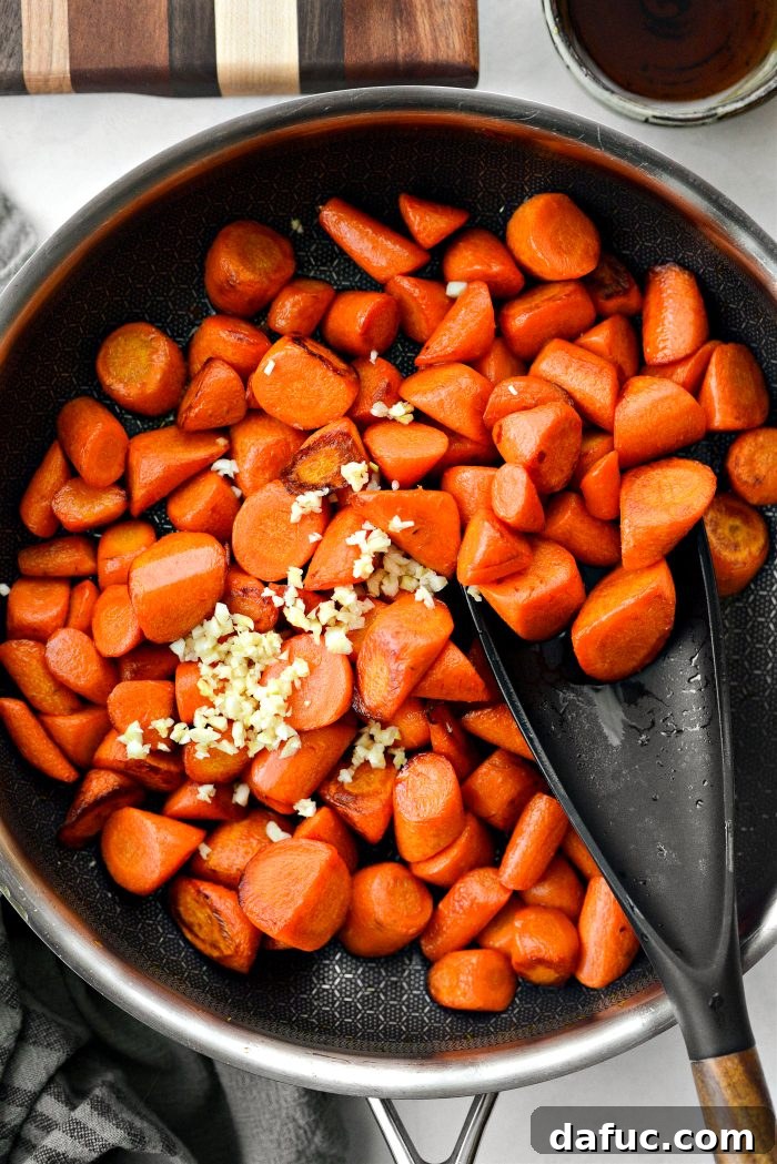 Adding minced garlic to fork-tender, caramelized carrots in a skillet