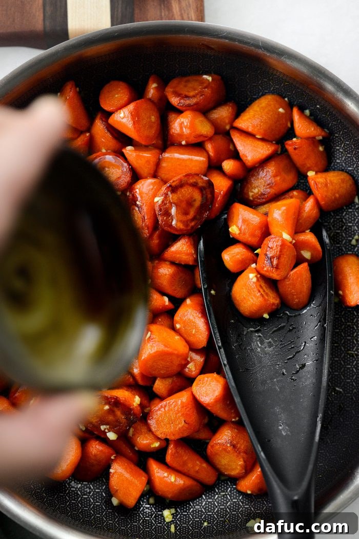 Pouring pure maple syrup over garlic-infused, caramelized carrots in a skillet