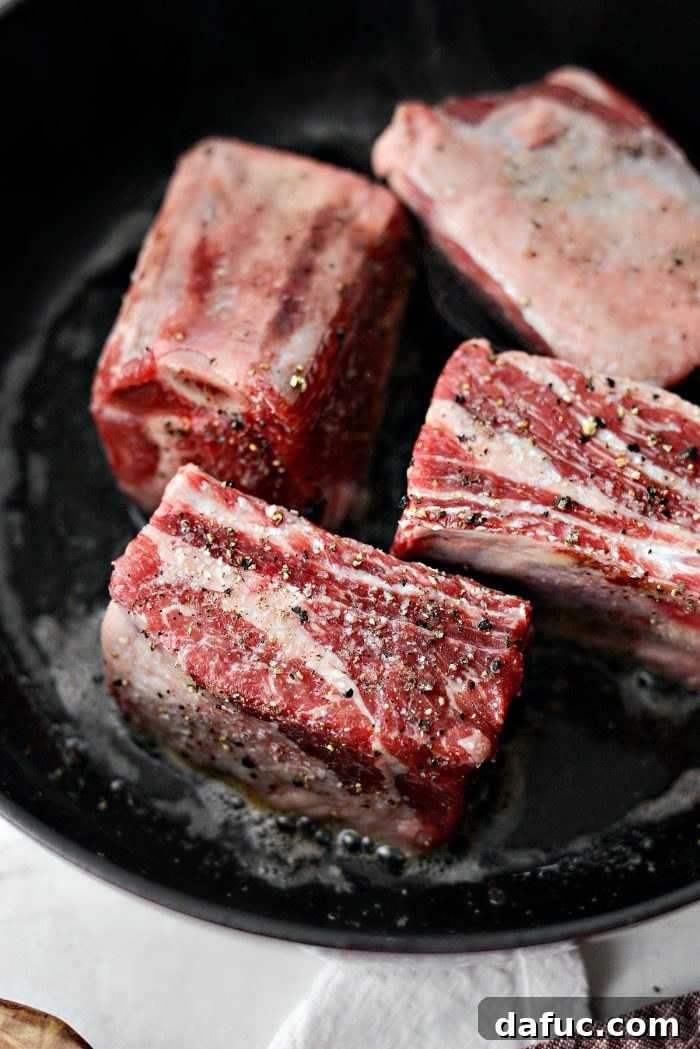 Slow-Braised Beef Short Ribs 7 Short ribs searing to a dark golden-brown in a hot pan with bacon fat, ensuring maximum flavor development.