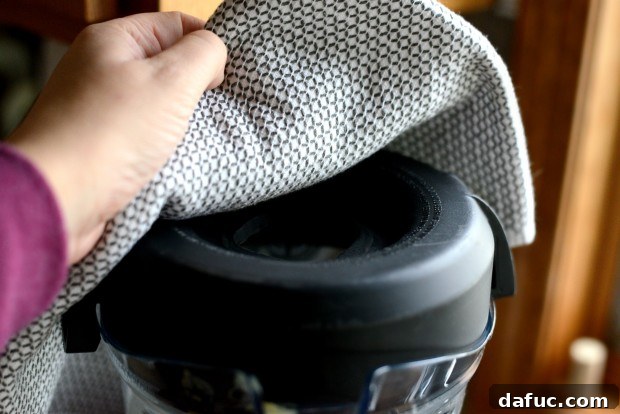 Blender with center plug removed, covered with a towel for safety