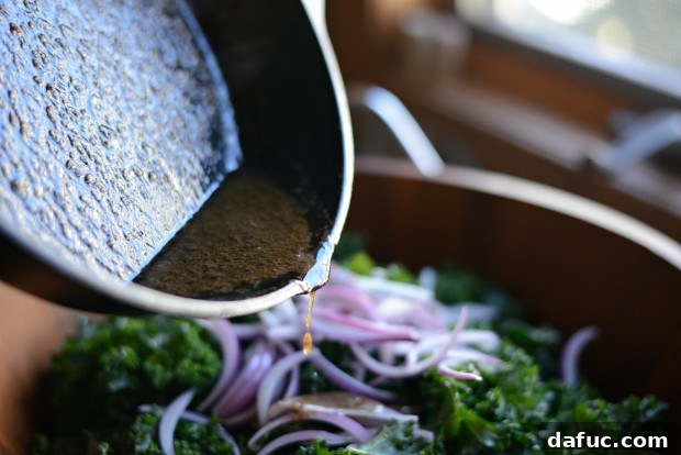 Hearty Winter Kale Salad with Crispy Pancetta and Blue Cheese Crostini 21 Hot pancetta fat dressing being poured over the kale and red onions in a large bowl.