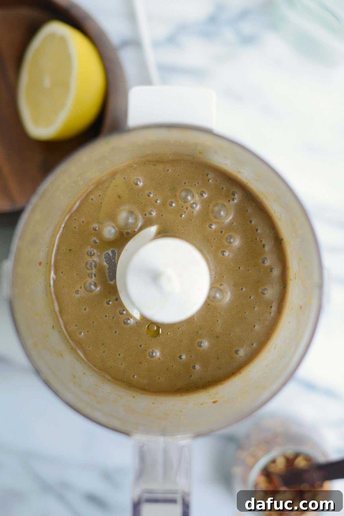 Olive oil being slowly poured into a food processor to emulsify vinaigrette