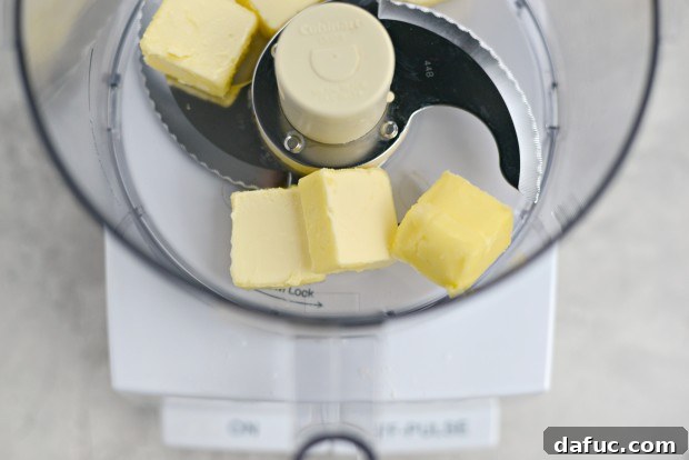 A young girl helping to pour ingredients into a food processor for the cookie dough