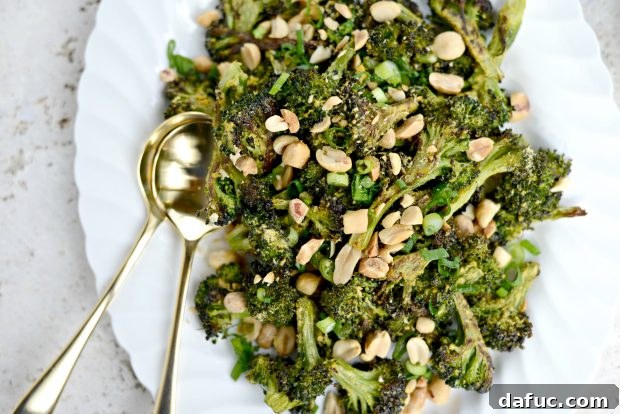 Savory Roasted Broccoli with Toasted Peanuts 2 Perfectly roasted broccoli florets with golden-brown edges, garnished with chopped peanuts and sliced green onions on a white plate.