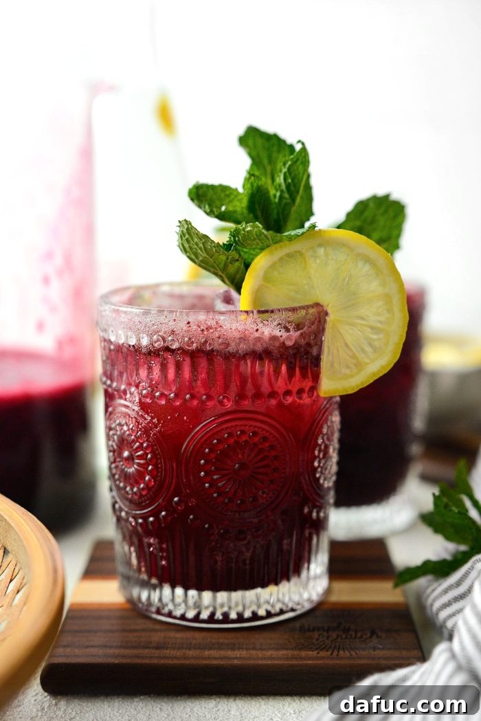 Glass of Blueberry Lemon White Wine Spritzer on a wooden table, garnished with mint and lemon