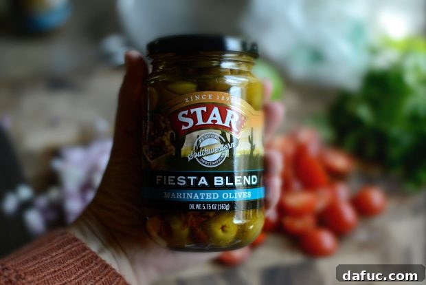 Grilled Red Snapper with a Vibrant Fiesta Olive Medley 4 Ingredients for the warm fiesta olive topping laid out on a cutting board, including STAR's Fiesta Blend Marinated Olives, cherry tomatoes, and fresh cilantro.