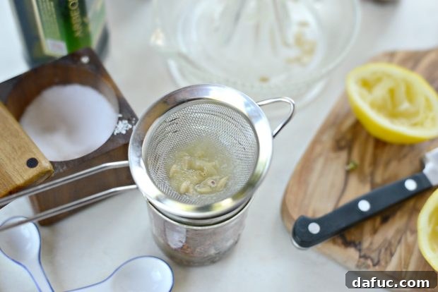Straining fresh lemon juice into the dressing jar to catch seeds