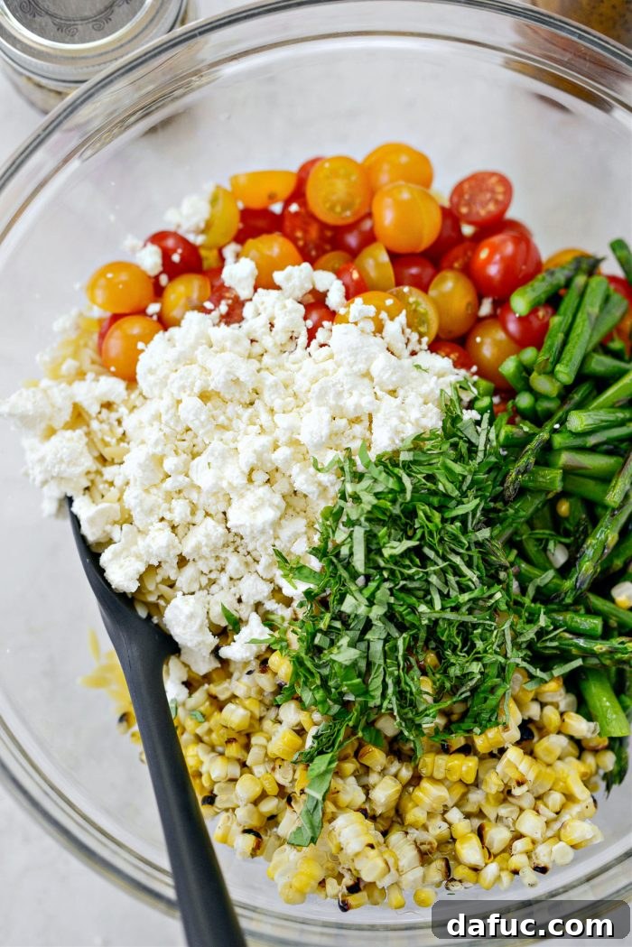 Vibrant Grilled Corn Orzo Salad 13 Adding crumbled feta cheese and thinly sliced fresh basil to the large mixing bowl of salad ingredients.