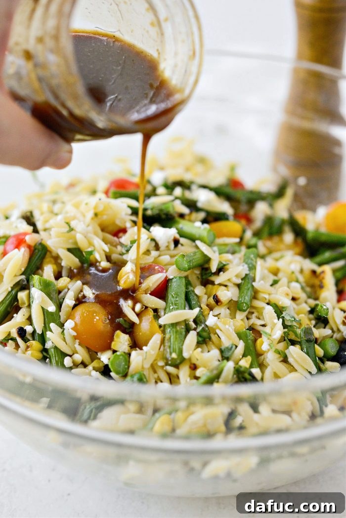 Vibrant Grilled Corn Orzo Salad 15 Pouring a portion of the balsamic vinaigrette over the mixed orzo pasta salad in the large bowl.
