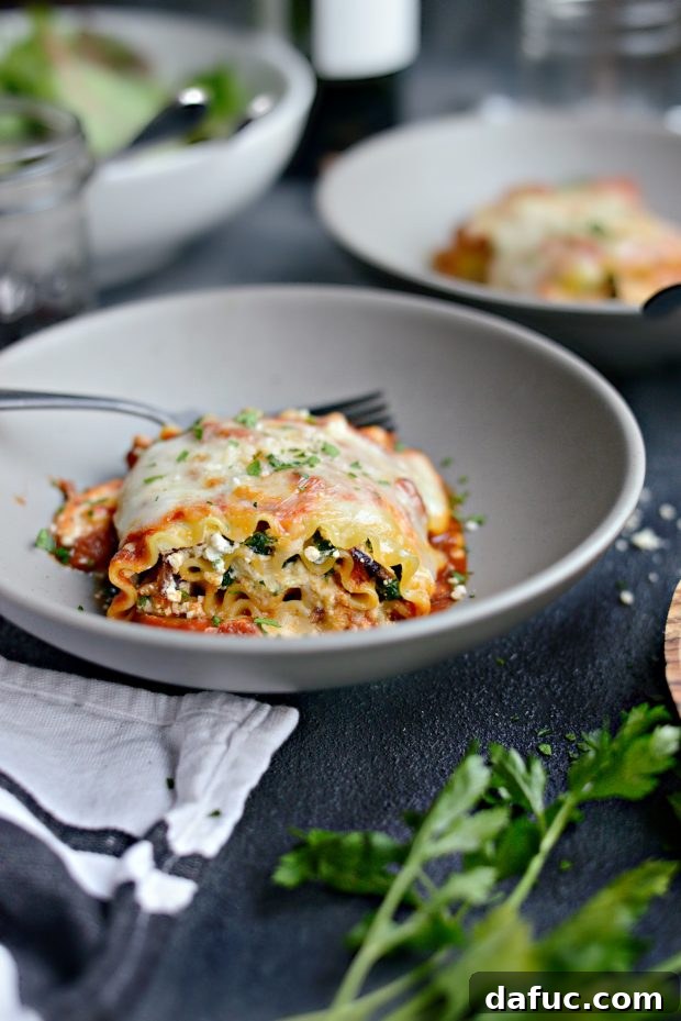 Lasagna roll-ups baking in a casserole dish, topped with sauce and cheese