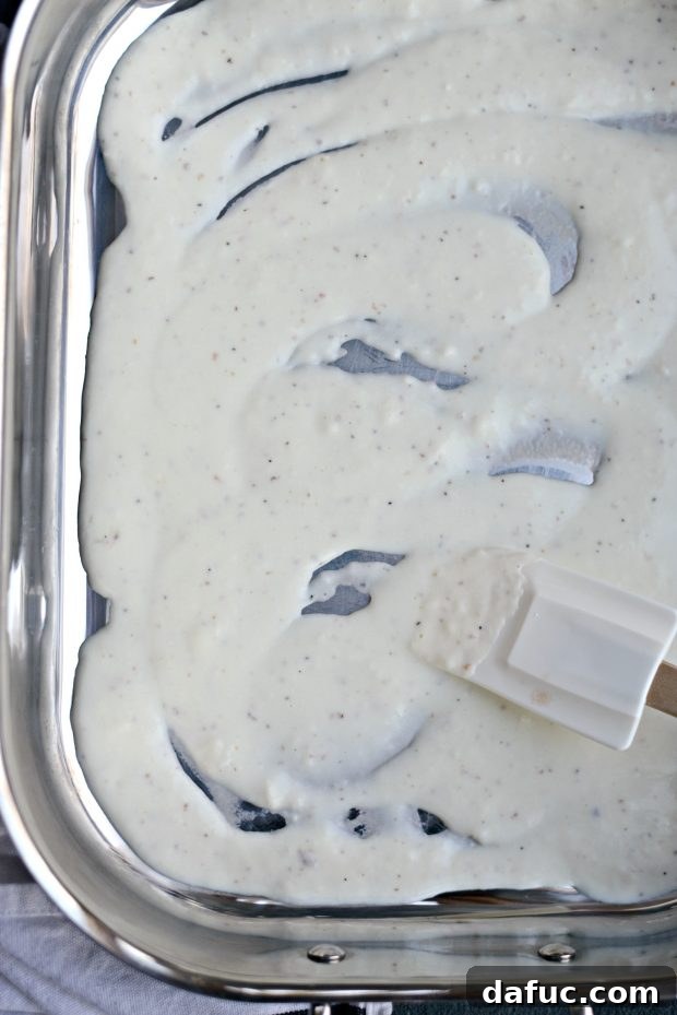 Creamy béchamel sauce poured into a lasagna pan, ready for the roll-ups