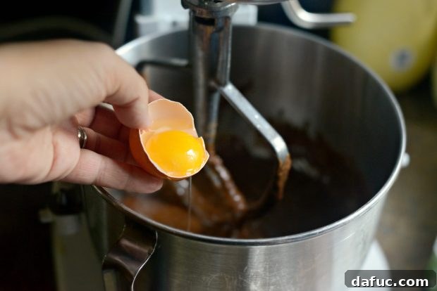 Adding eggs one by one to chocolate cake batter in a stand mixer