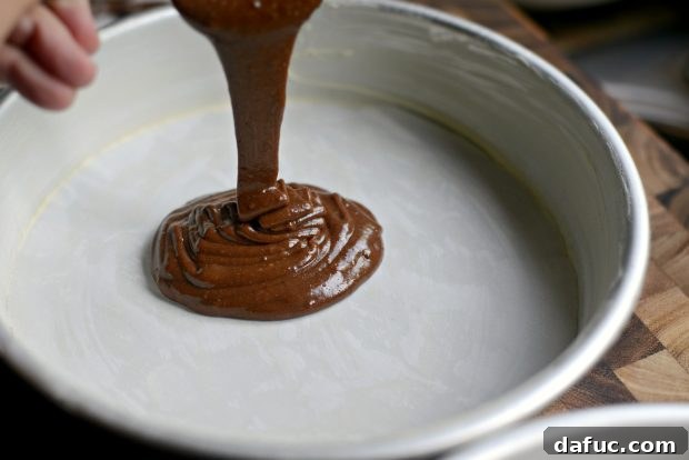 Dividing chocolate cake batter evenly between two prepared cake pans