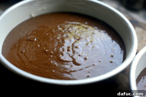 Chocolate cake batter settling in prepared cake pans before baking