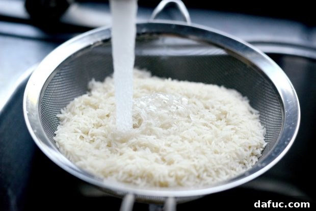 Effortless Rice Cooker Coconut Rice 4 Basmati rice being rinsed under cool running water in a mesh strainer until the water runs clear.