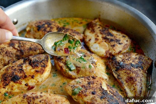 Spoon sauce over chicken - Cooked chicken pieces being covered with the creamy cilantro lime sauce in a skillet.