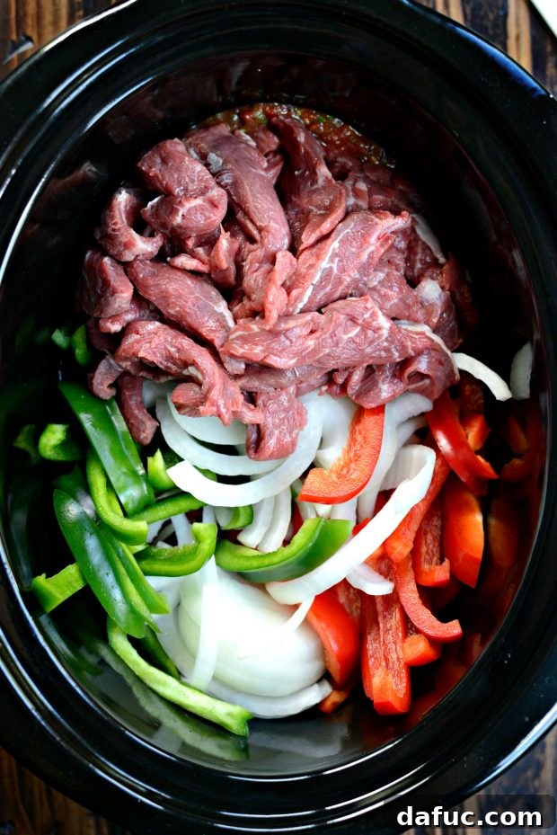Adding sliced beef, onions, and bell peppers into the slow cooker over the salsa