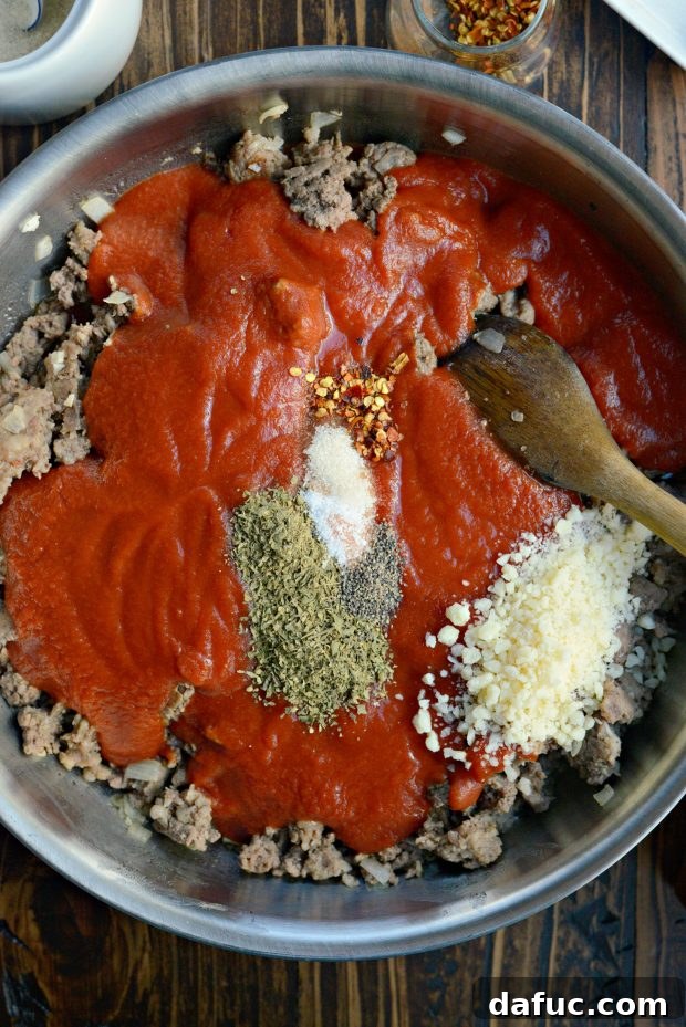 Adding tomato sauce, herbs, and Parmesan cheese to cooked meat mixture