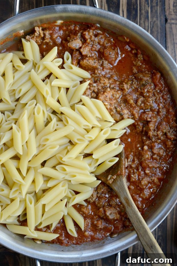 Adding partially cooked pasta to the meat sauce in the pan