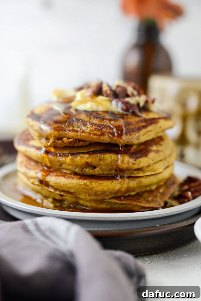 Spiced Brown Butter Pumpkin Pancakes 15 A plated serving of Brown Butter Pumpkin Pancakes, beautifully garnished with melting butter, a generous pour of maple syrup, and a sprinkle of chopped toasted pecans.