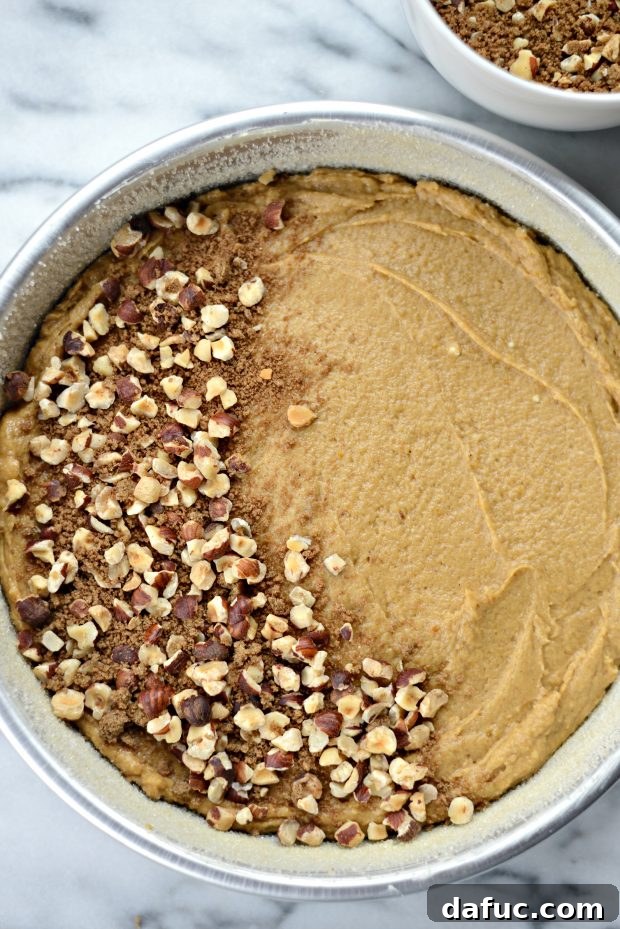 Sprinkling hazelnut streusel topping over pumpkin coffee cake batter