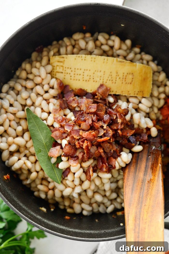 Smoky Bean and Bacon Delight 14 Adding navy beans, half of the crispy bacon, Parmesan rind, and bay leaf to the pot, establishing the core components of the soup.
