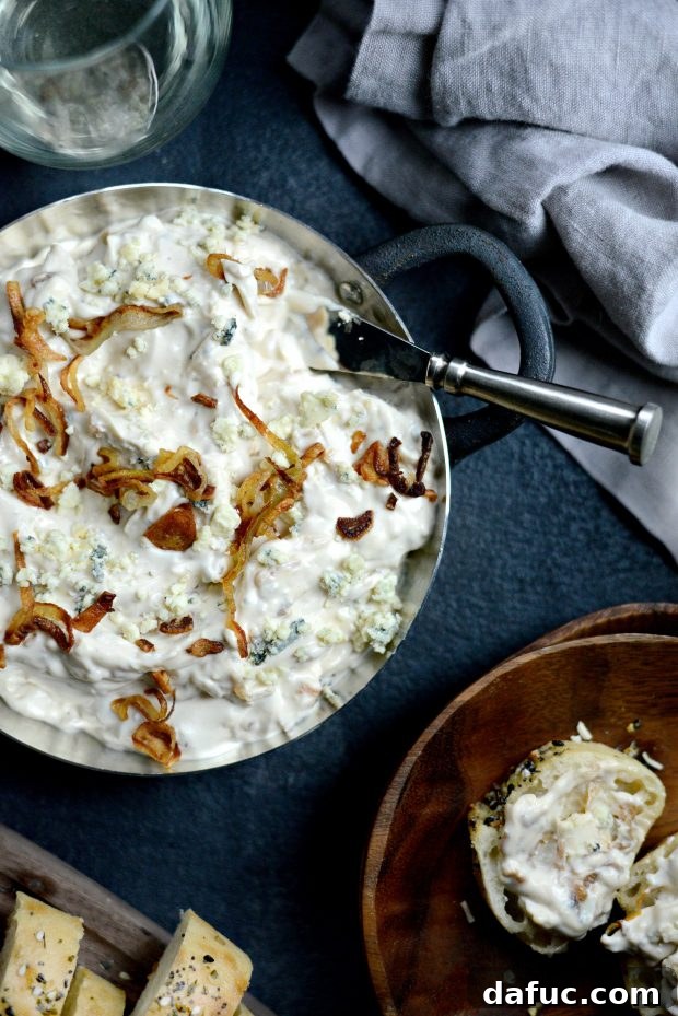 Sweet and Tangy Blue Cheese Shallot Dip 16 Hand holding a slice of baguette with Caramelized Shallot and Blue Cheese Dip, ready to be eaten.